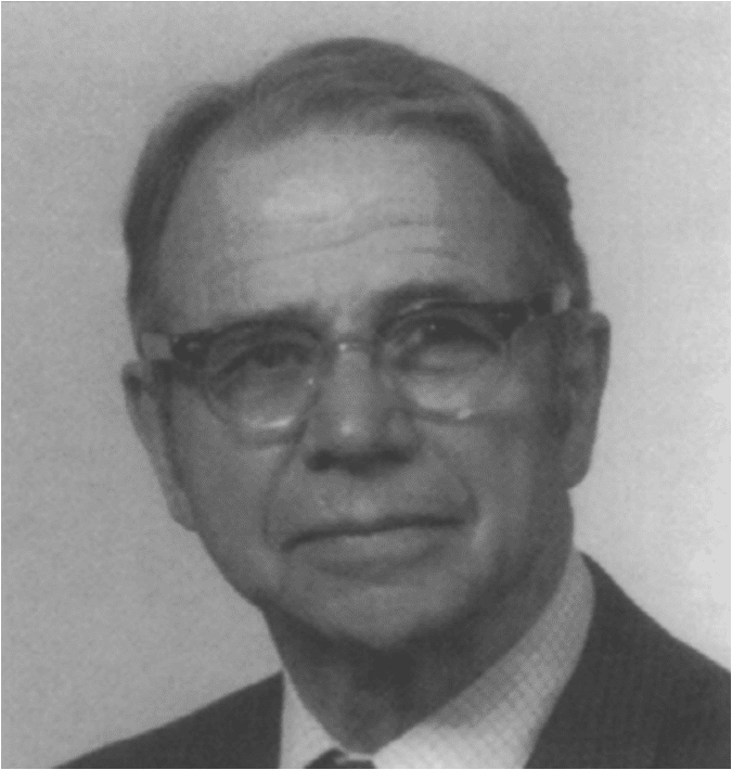 Richard Hartshorne posing and wearing a white striped suit and tie along with his eyeglasses.