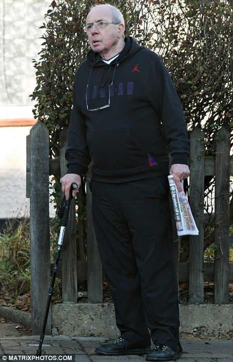 Richard O'Sullivan wearing eyeglasses, black hoodie, black pants and black shoes while holding a cane.