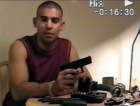 Ricky Rodriguez holding a gun while wearing a maroon shirt
