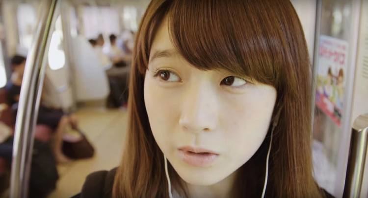 Rie Kaneko looking at something while at the train and wearing an earphone