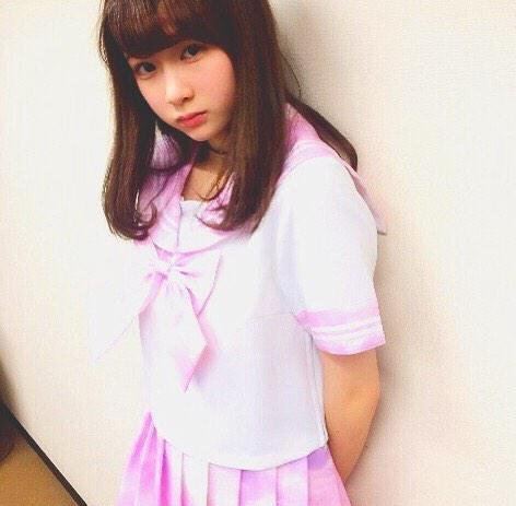 Rie Kaneko leaning on a wall and wearing a white uniform with a oink collar and pink skirt