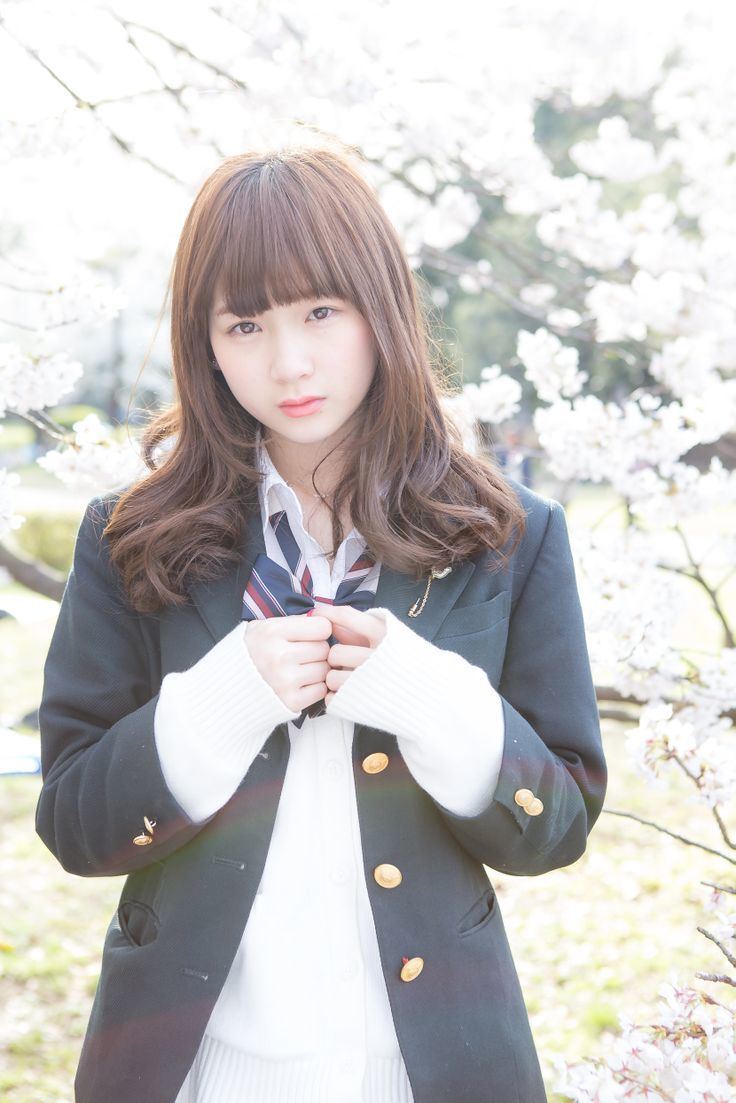 Rie Kaneko looking fierce and wearing a white blouse under a gray coat and a colored ribbon