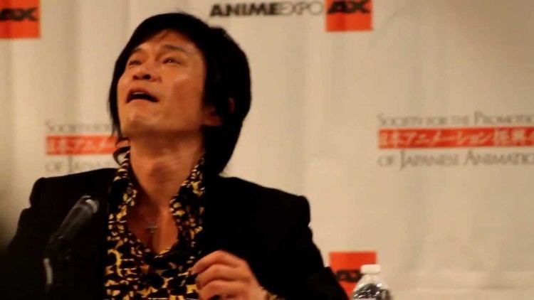 Rikiya Koyama, in a press conference, wearing a black coat and brown and black long sleeves