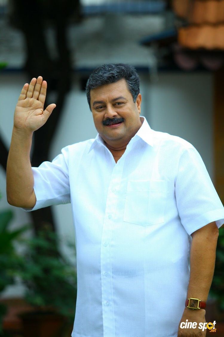 Rizabawa smiling with his mustache and raising his right hand while wearing a white shirt