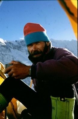 Rob Hall smiles while on top of the mountain wearing a thick jacket and hat