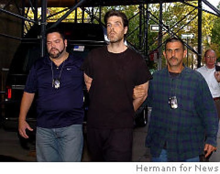 Robert Chambers and the two men beside him are looking afar with a serious faces, a mustache, and beards. Robert is wearing a black t-shirt and black pants, the man on his left is wearing a blue t-shirt, police id, and denim pants, and the man on his right is wearing a blue and green polo, police id, and denim pants