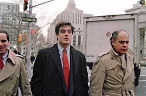 The man (left) is walking with Robert Chambers, the so-called "preppie killer," and his father, Robert Chambers Sr. (right) heading to New York City Criminal Court, on December 12, 1986, with serious faces. The man (left) is wearing a blue long sleeve under a red necktie and a beige coat. Robert Chambers Jr is wearing a blue long sleeve under a red necktie and a black coat. Robert Chambers Sr. is wearing a beige trench coat