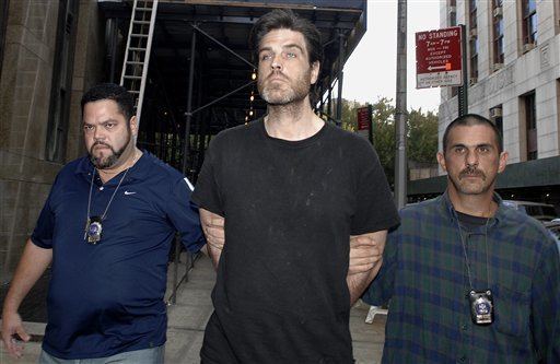 Robert Chambers and the two men beside him are looking afar with a serious faces, a mustache, and beards. Robert is wearing a black t-shirt, the man on his left is wearing a blue t-shirt and police id, and the man on his right is wearing a blue and green polo and police id