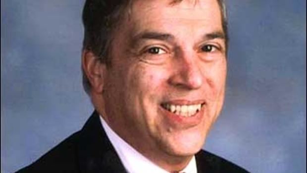 Robert Hanssen with a big smile while wearing a black coat and white long sleeve