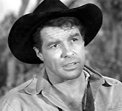 Robert Horton as Flint McCullough looking afar with a serious face in a scene from the 1957 movie "Wagon Train", wearing a shirt and a hat