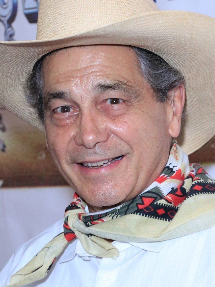 Robert L. Crawford Jr. smiling, wearing a light brown hat, white long sleeves, and colorful scarf.