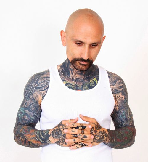 Robert LaSardo looking down while crossing his hands, with mustache and beard, and he is wearing a white sando