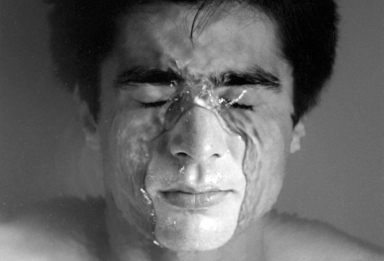 Javier, 1985, captured by Robert Mapplethorpe, half of a man's face is under the water while his eyes are closed and he is topless