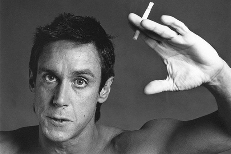 Iggy Pop raising his hands while holding a cigarette with a serious face and topless, 1981, captured by Robert Mapplethorpe