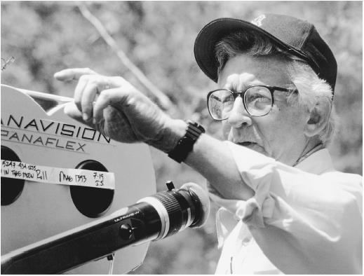 Robert Mulligan looking afar while pointing at something on the set of the 1991 American coming of age drama film, The Man in the Moon. Robert is wearing a cap, eyeglasses, wristwatch, and long sleeve