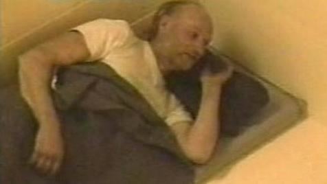 Robert Pickton lying on the bed and wearing a white t-shirt
