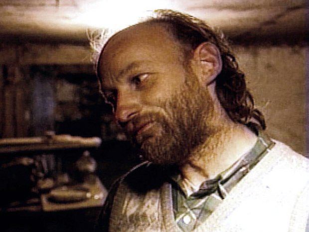 Robert Pickton looking at something while wearing a white sweater vest and green checkered polo