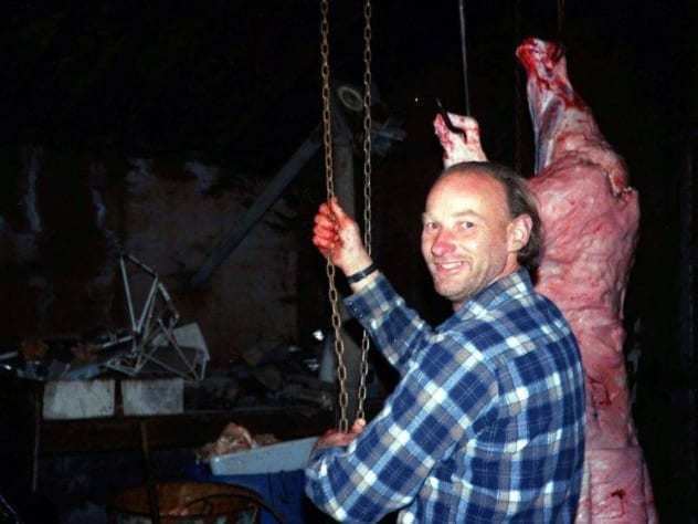 Robert Pickton holding a chain and a pig's dead body beside him while he is wearing a blue checkered long sleeves