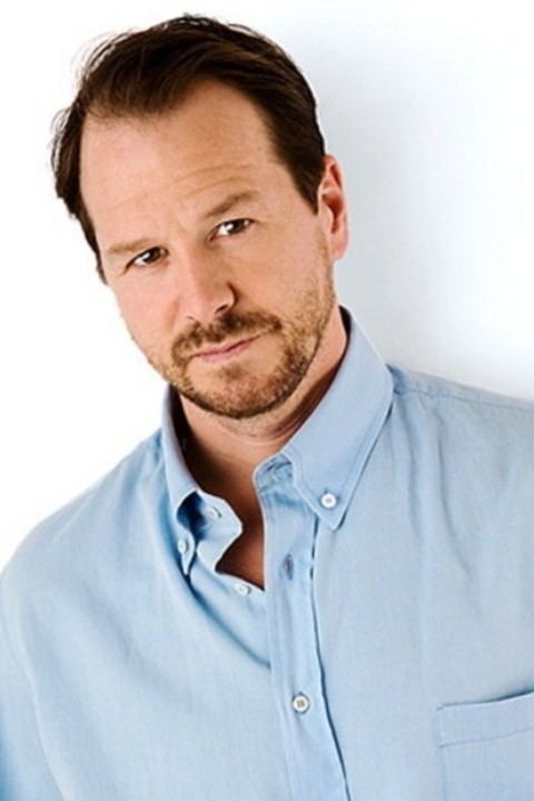 Robert Wahlberg with a tight-lipped smile, mustache, and beard while wearing a light blue long sleeves