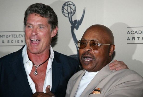 David Hasselhoff talking to someone while wearing a black coat and long sleeves while Roger E. Mosley wearing a gray coat and eyeglasses