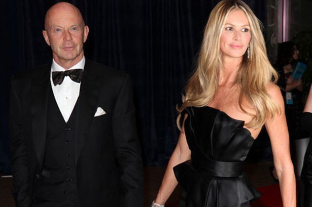 Roger Jenkins (left) is serious, and bald, left hand holding the hand of Elle, he wears white long sleeves, a black bow tie under a black suit with a pocket on his left with a handkerchief inside. Elle Macpherson (right) is smiling, and has long blonde hair, her right hand holding the hand of Roger, she wears a silver bracelet in her right hand, silver earrings, and a black off-shoulder sexy dress.