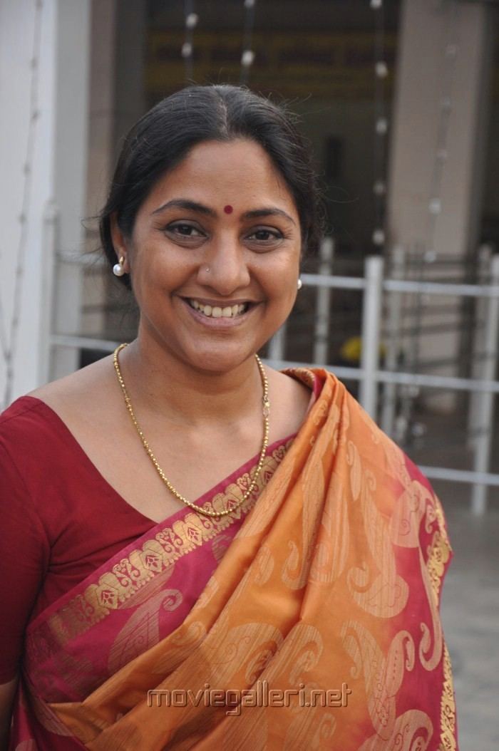 Rohini in a wide smiling pose with a red dot on her forehead while wearing a red saree, pearl earrings, and gold necklace