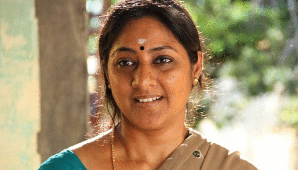 Rohini smiling with a black mark on her forehead while wearing a blue dress and brown shawl