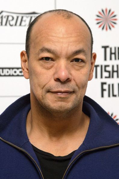 Roland Gift smiling while wearing a blue jacket and black inner shirt