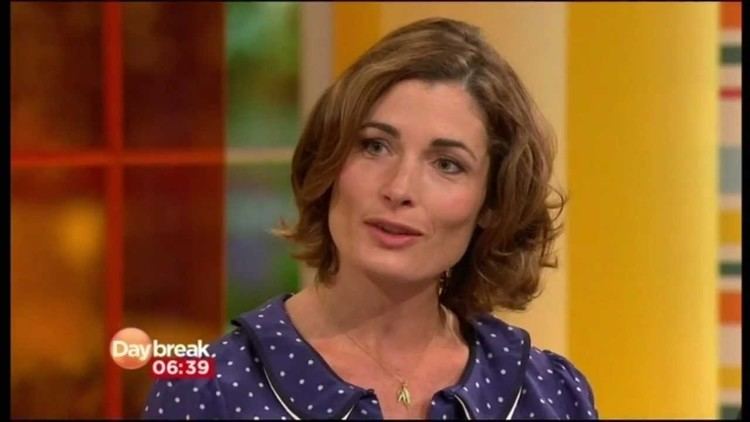 Romilly Weeks talking in an interview in the Daybreak segment and wearing a polka dot purple blouse & a necklace.