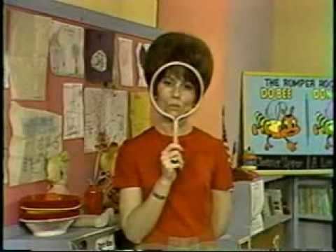 Miss Barbara in Romper Room wearing a red shirt while holding a white circled object.