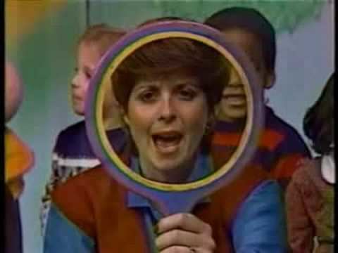 Miss Barbara in Romper Room wearing a blue and red shirt while holding a circled object.