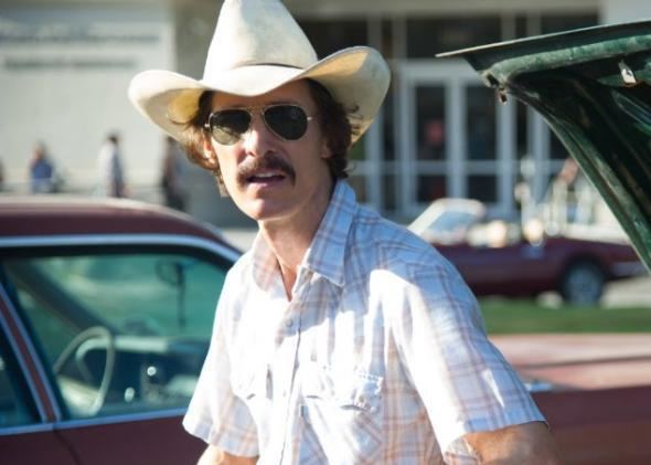 Matthew McConaughey with a mustache, wearing a hat, sunglasses, and checkered polo shirt who played the role of Ronald Dickson Woodroof in the film Dallas Buyers Club.
