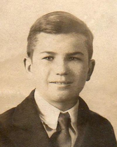 Young Ronald Speirs smiling while wearing a coat, long sleeves, and necktie