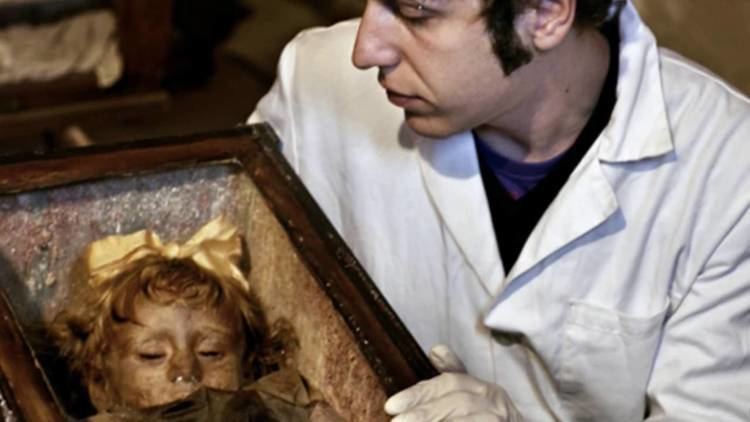 Dario Piombino Mascali poses in front of the mummified body of Rosalia Lombardo, who died at the age of two from pneumonia and is preserved inside the Capuchin Catacombs of Palermo.