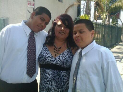 Rosalie Garcia smiling in the center and wearing a black and white dress and necklace with her sons Andrew and Nicholas wearing white long sleeve shirts and neckties