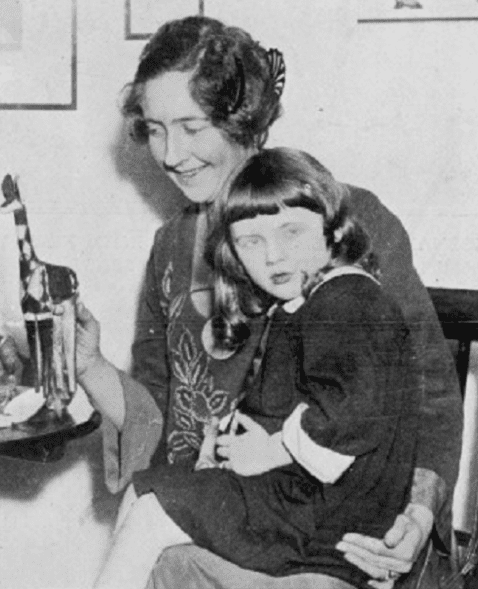 Agatha Christie smiling while looking at the animal stuffed toy at the table and her daughter Rosalind Hicks sitting on her lap