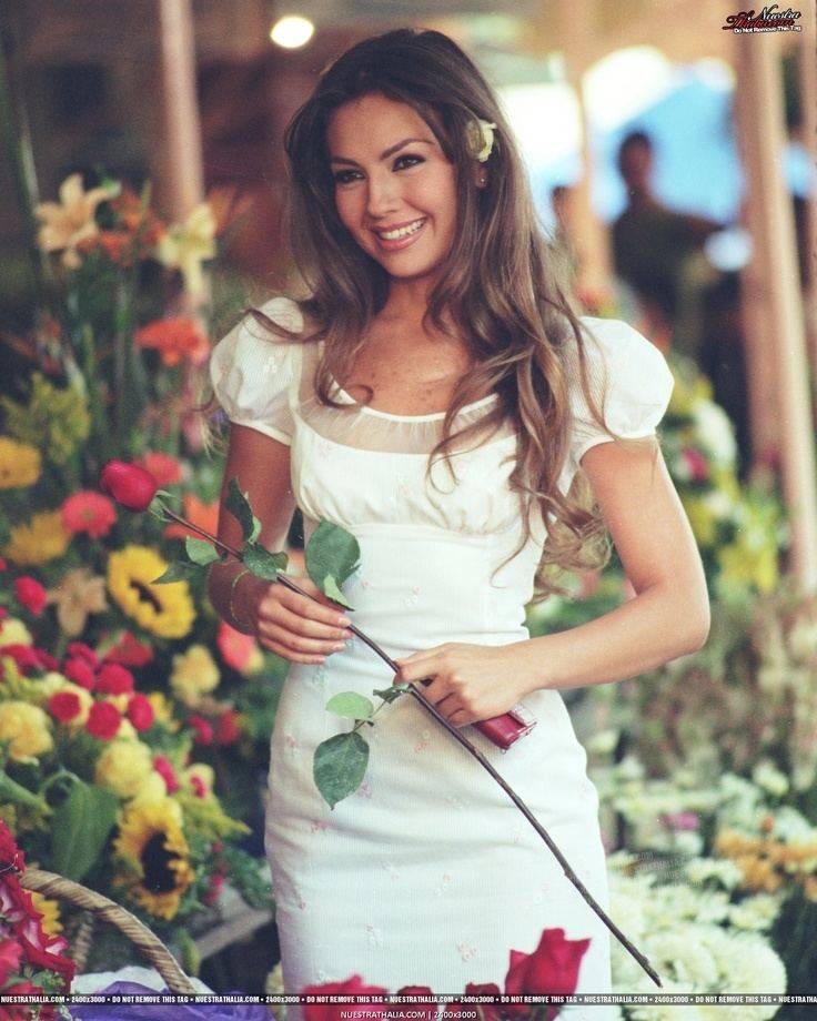 Thalía as Rosalinda, smiling while holding a red rose and wearing a white dress