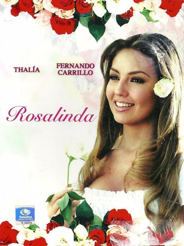 Thalía as Rosalinda, smiling while holding a white rose and another white rose is on her ear and she is wearing a white dress