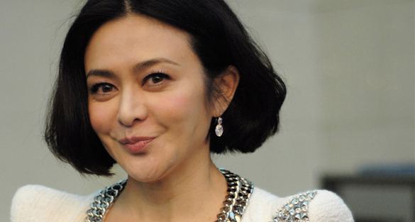 Rosamund Kwan smiling while wearing a white blouse and earrings