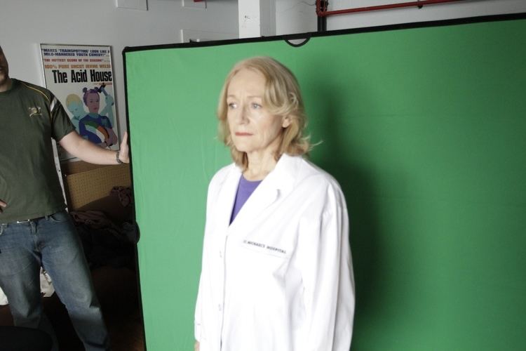 Rosemary Dunsmore standing in front of a green backdrop while wearing a white coat and purple blouse