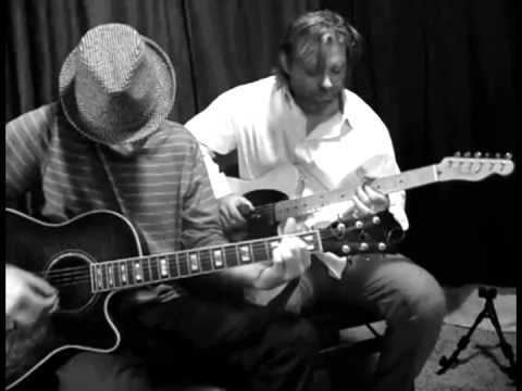 Ross Childress playing the guitar while wearing a hat and striped shirt and the man behind him wearing white long sleeves