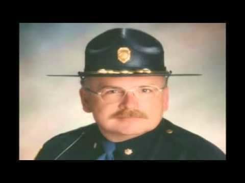 A man with mustache wearing police cap, eyeglasses and black jacket