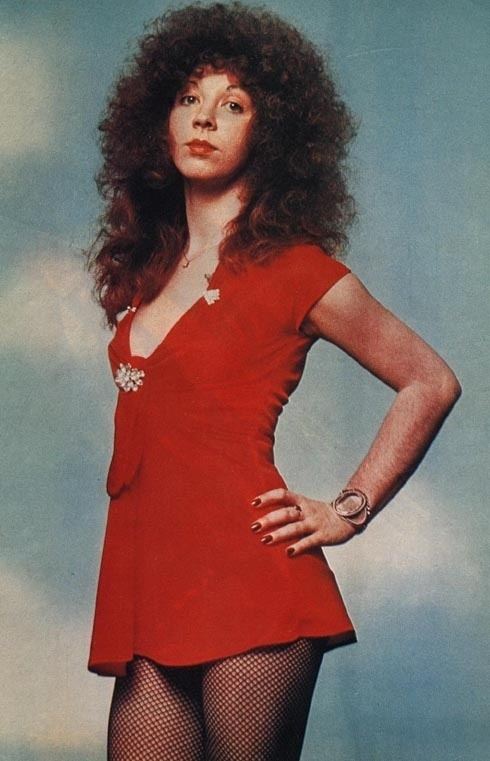 Ruby Starr with curly hair, wearing a necklace, bracelet, a ring, and a sexy red dress