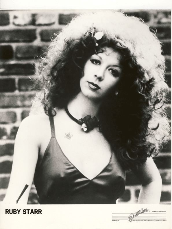 Ruby Starr with curly hair, wearing a necklace and a sexy top.