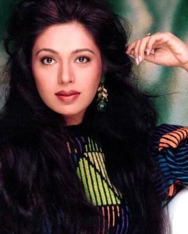 Rupini with a tight-lipped smile while wearing a striped blouse and earrings