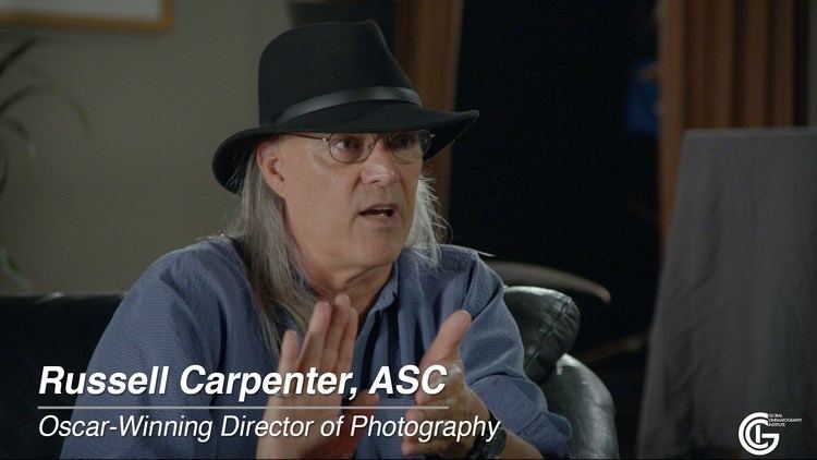 Russell Carpenter, in one of his interviews, wearing a black hat, eyeglasses, and blue long sleeves
