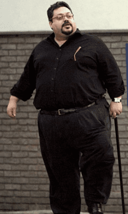 Russell King walking with a cane, wearing eyeglasses, a watch, a black long sleeve shirt, and black pants