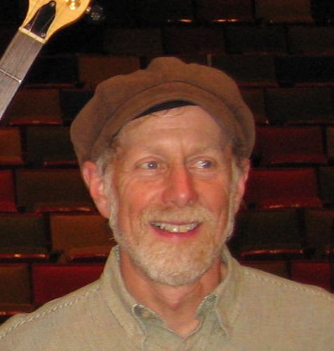 Rusty Jacobs smiling with mustache and beard while wearing a beige long sleeves and brown hat