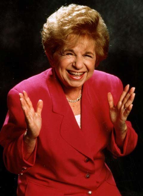 Ruth Westheimer laughing while wearing red coat and necklace