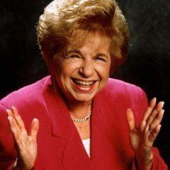 Ruth Westheimer laughing while wearing red coat and necklace